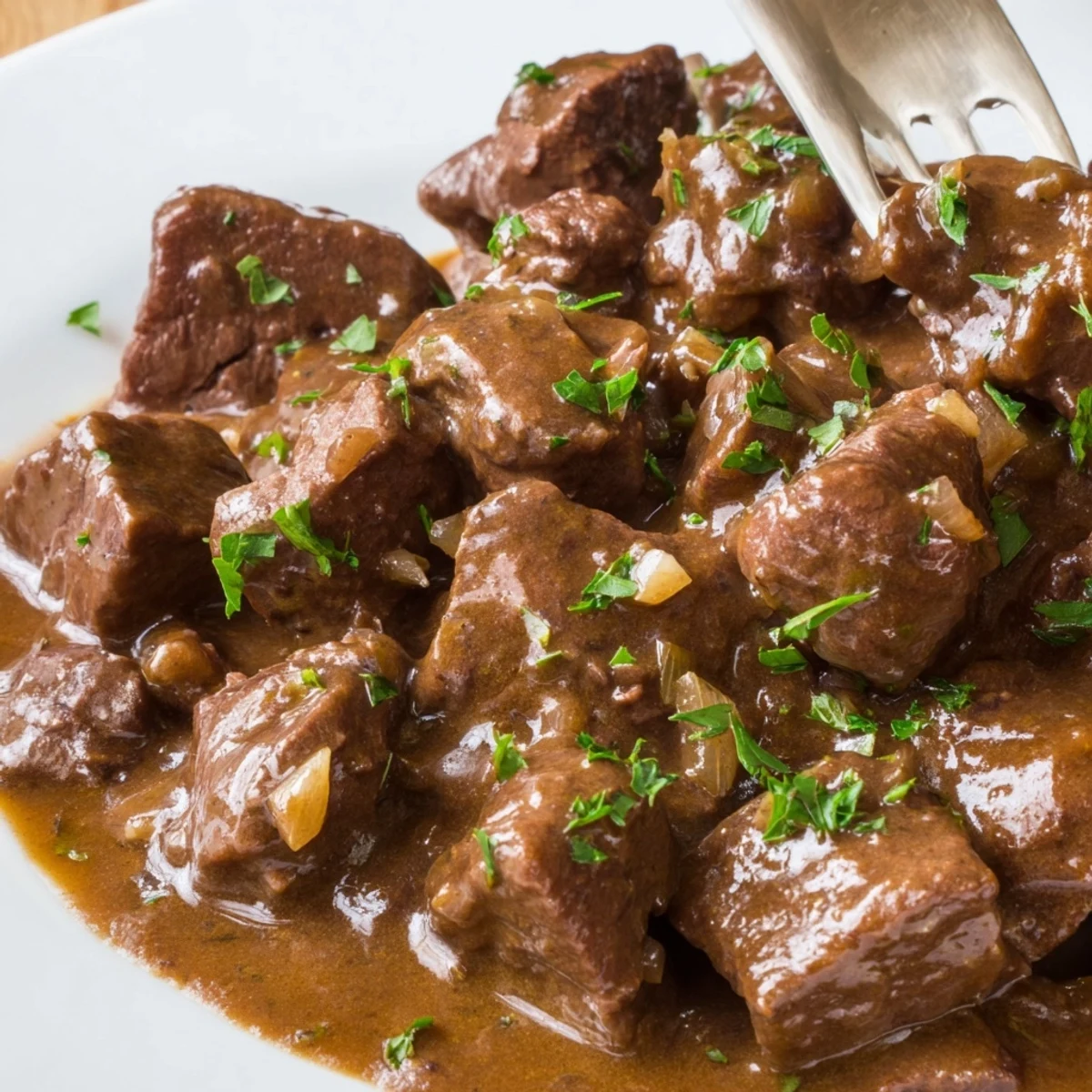Tender beef tips and gravy recipe served with fresh parsley garnish on white ceramic plate