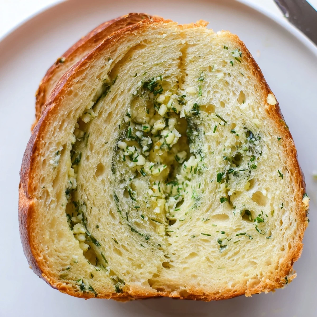 Garlic and herb bread loaf on cutting board with knife positioned beside golden crust and fresh green herb garnish