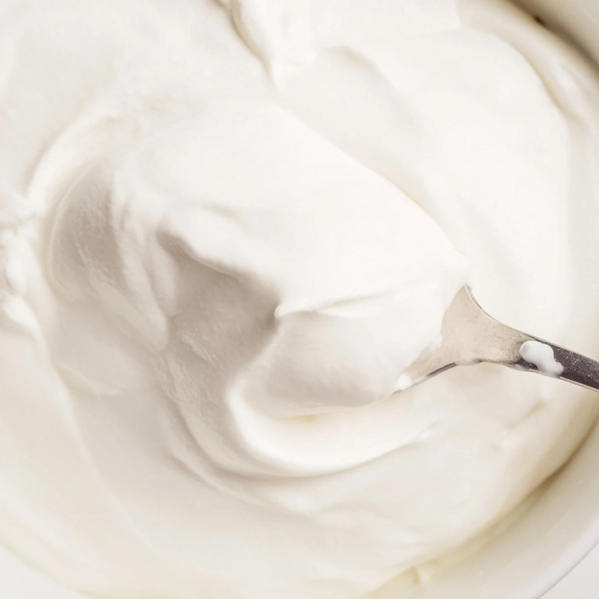 Spoonful of rich tangy Greek yogurt garnished with walnuts and cinnamon on wooden board