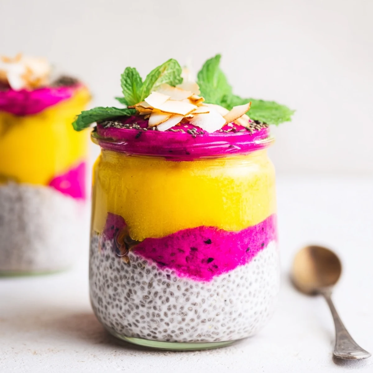 Vibrant layered mango and dragon fruit chia pudding in glass jars topped with fresh mint
