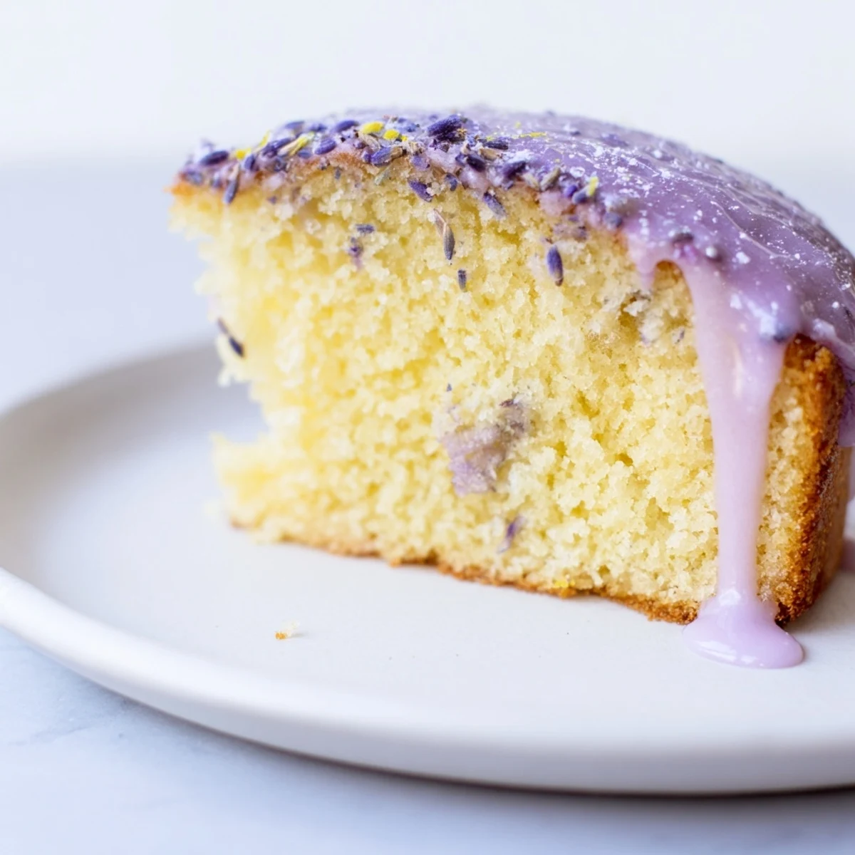 A slice of lavender cake with lemon glaze drizzled over the golden crumb