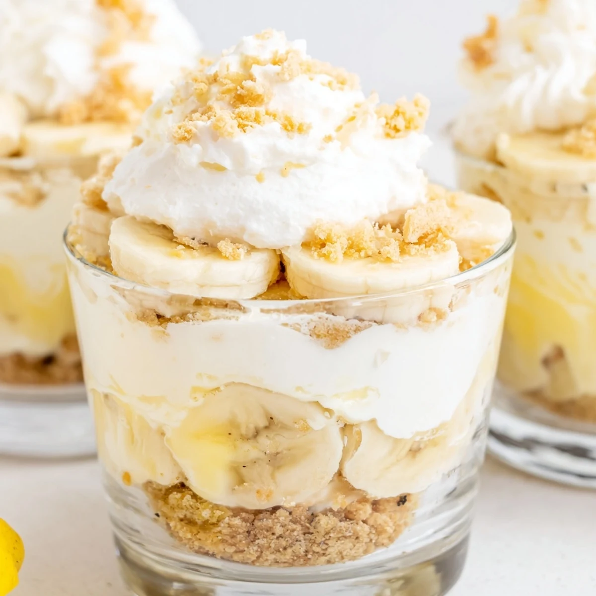 Creamy No Bake Banana Pudding Cheesecake Cups layered in clear glass jars with vanilla wafer crumbs