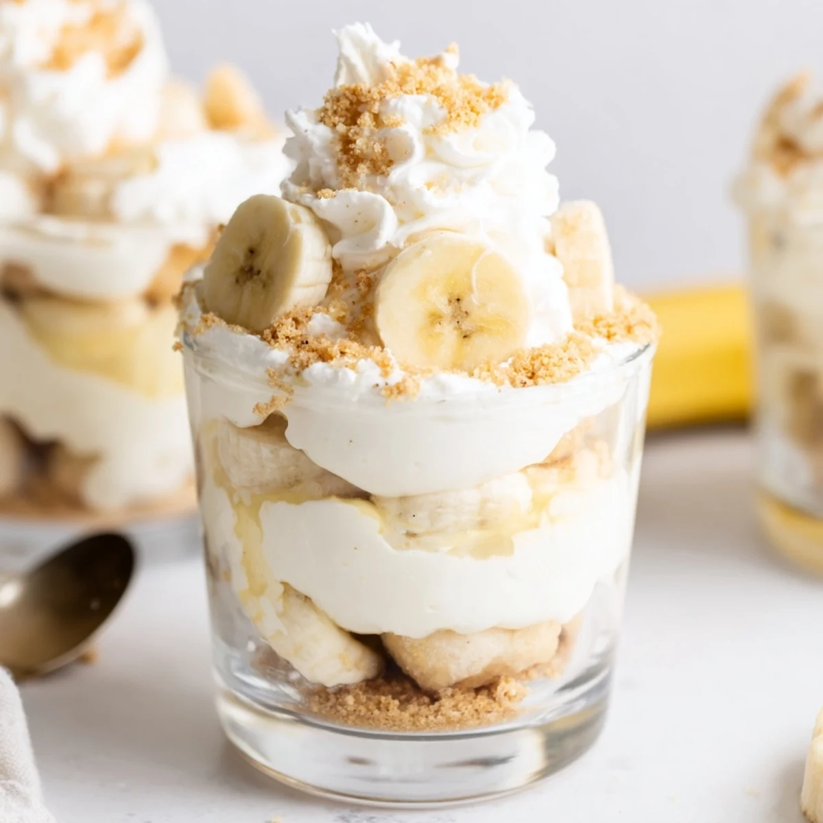 No Bake Banana Pudding Cheesecake Cups topped with fresh banana slices and crunchy cookie crumbles