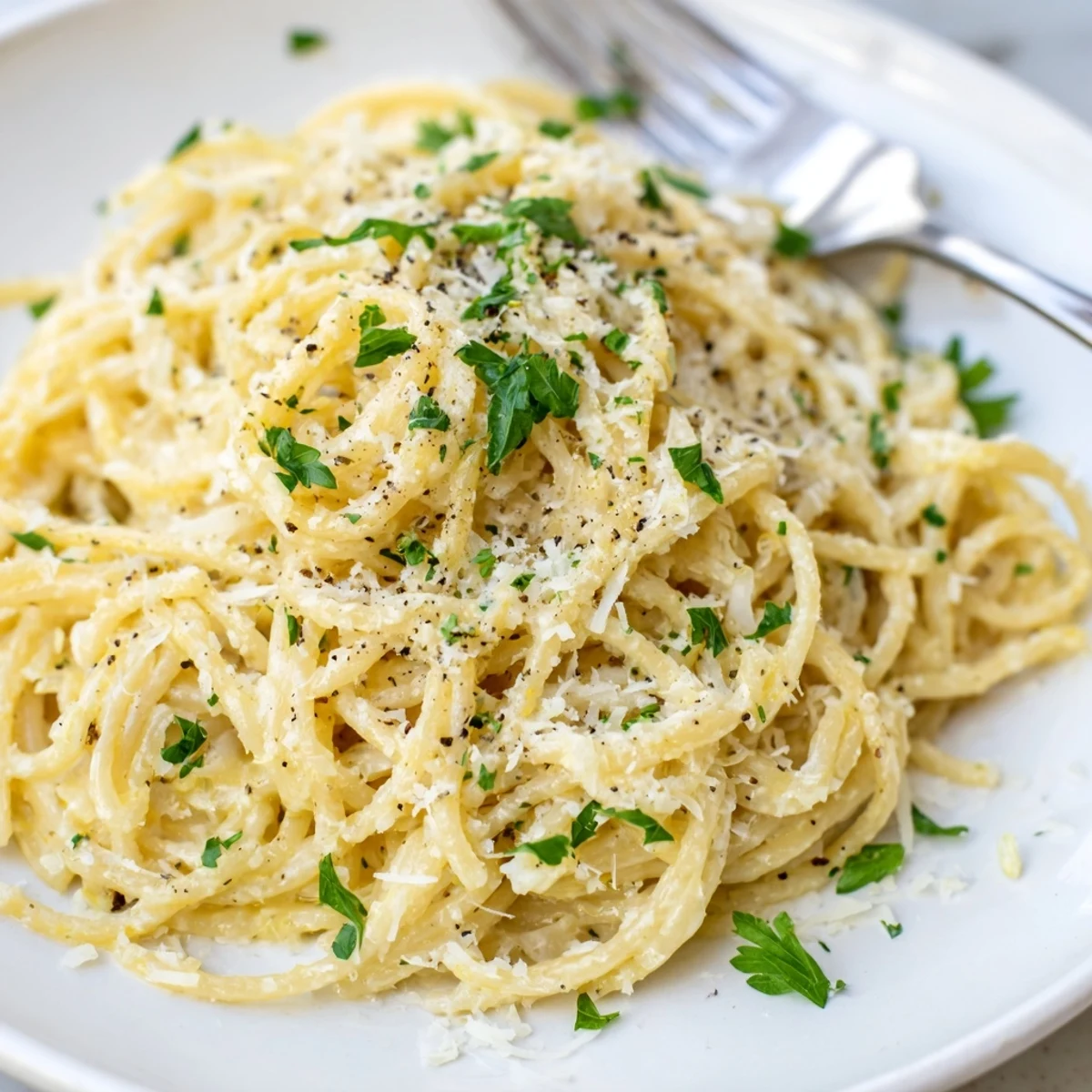 Creamy Parmesan lemon pasta twirled on a fork with fresh herbs and black pepper sprinkled on top
