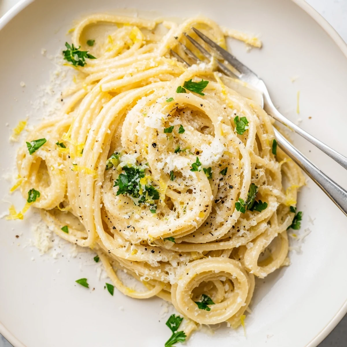 Golden buttery Parmesan lemon pasta served in a white bowl with zest and extra cheese garnish