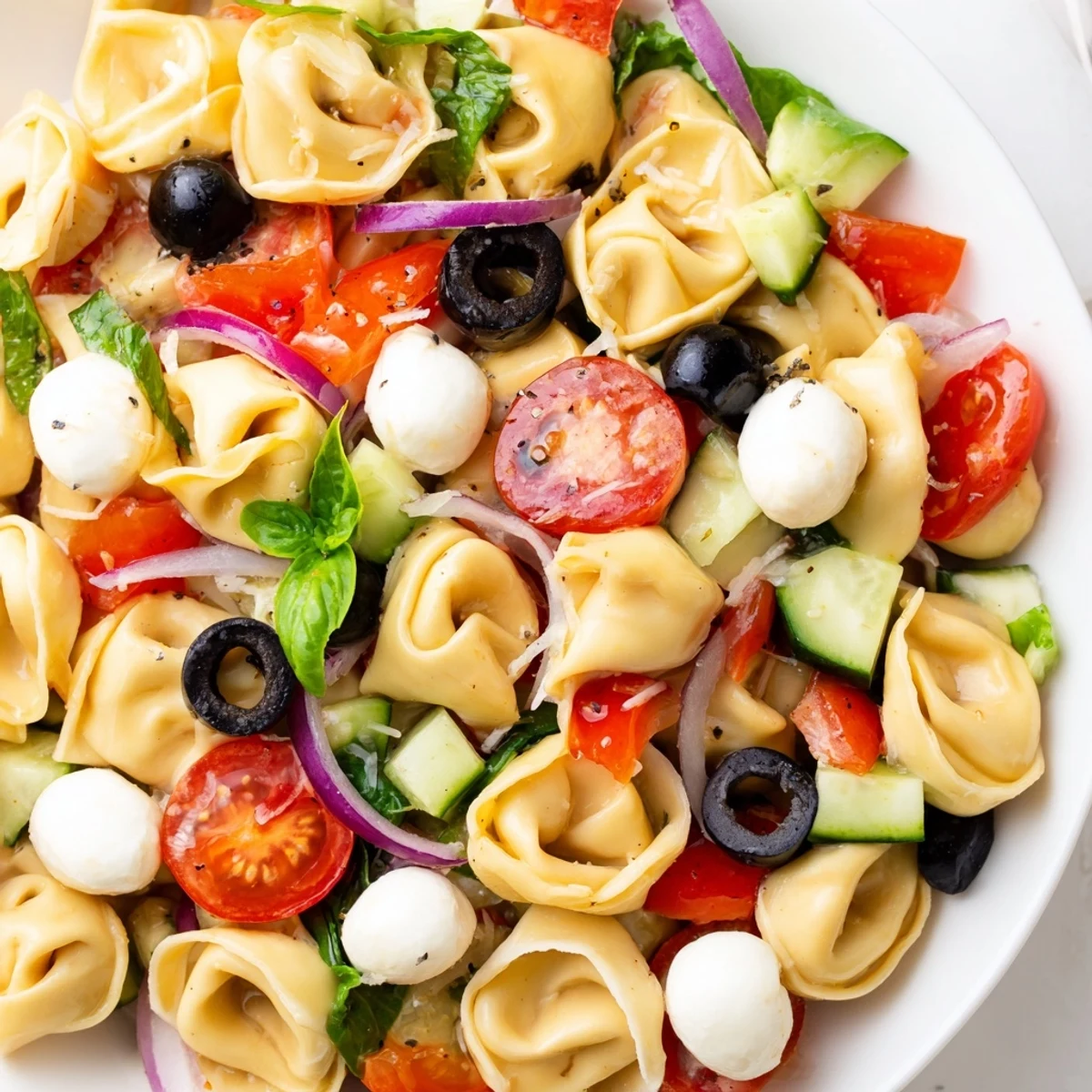 Colorful tortellini salad with cherry tomatoes, cucumber, and zesty Italian dressing in a serving bowl