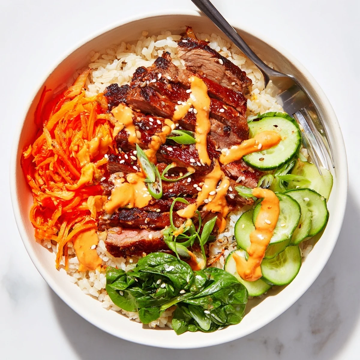 Korean BBQ steak rice bowls topped with crisp veggies and creamy sriracha drizzle