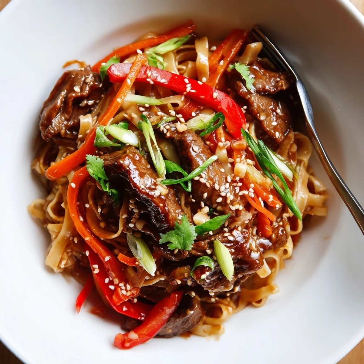 Warm Sticky Beef Noodles steaming on plate, garnished with sesame seeds