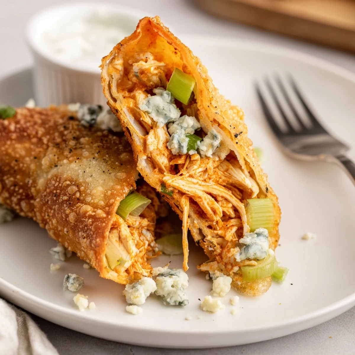 Crispy Buffalo Chicken Egg Rolls steaming on plate, celery and blue cheese