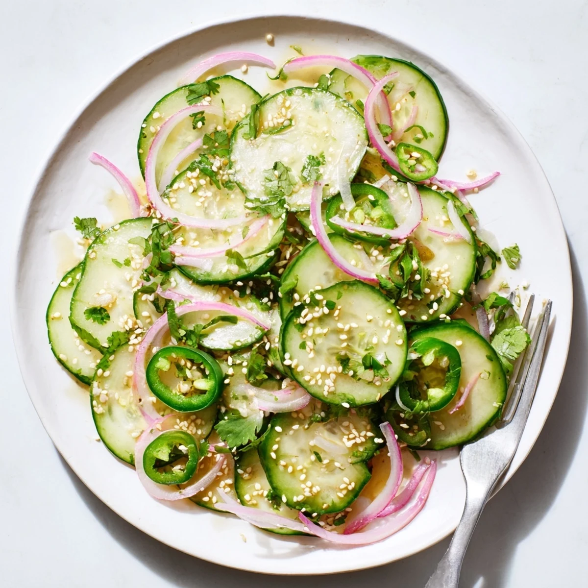 Vibrant green cucumber salad drizzled with honey lime dressing and topped with fresh cilantro in a white bowl