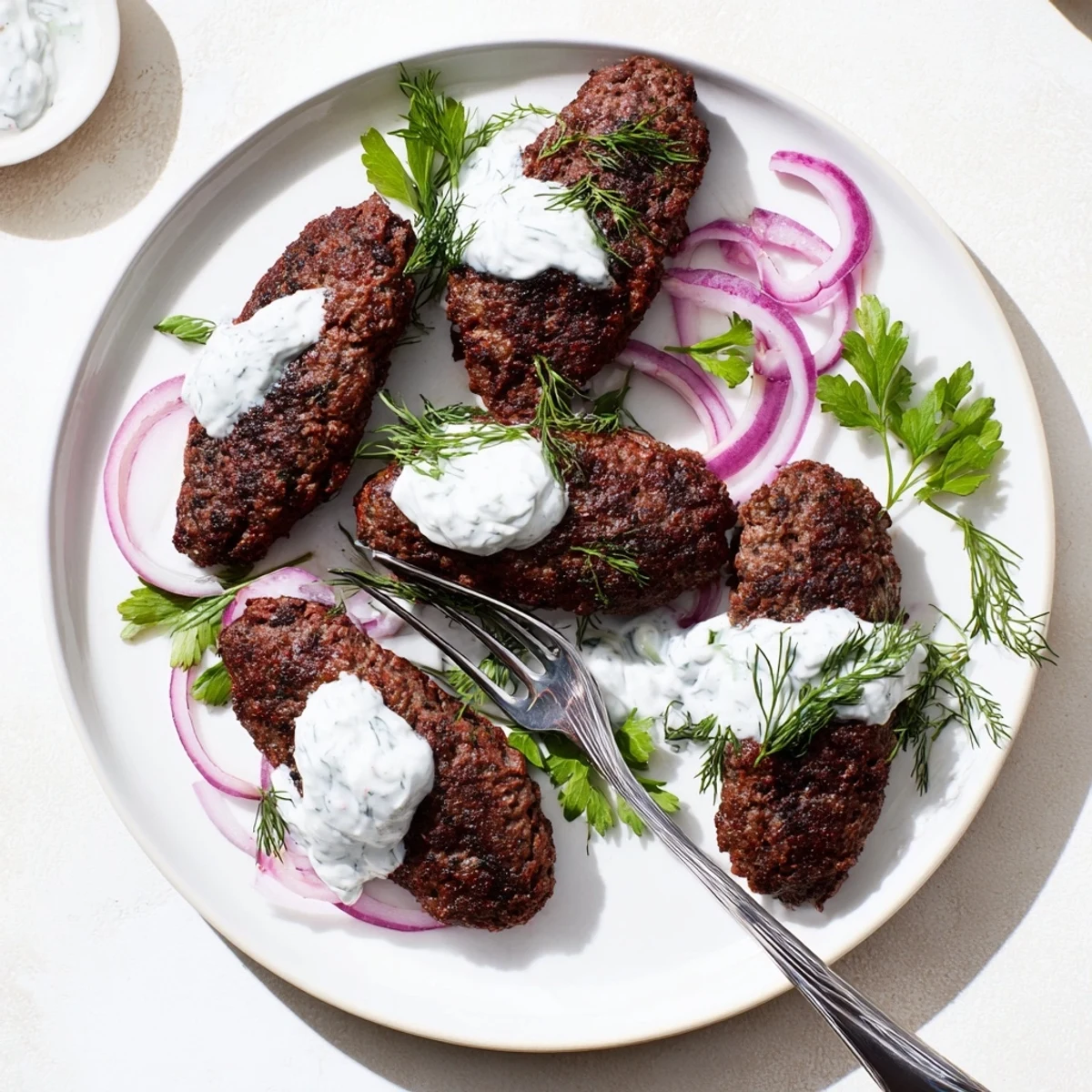 Golden smashed beef kebabs with crispy edges served alongside creamy cucumber yogurt sauce