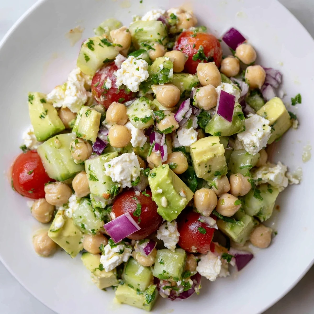 Colorful chickpea feta avocado salad topped with crumbled cheese and fresh parsley