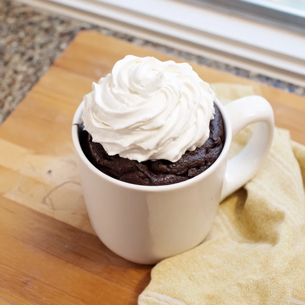 A steaming gluten free chocolate mug cake topped with whipped cream and fresh raspberries.